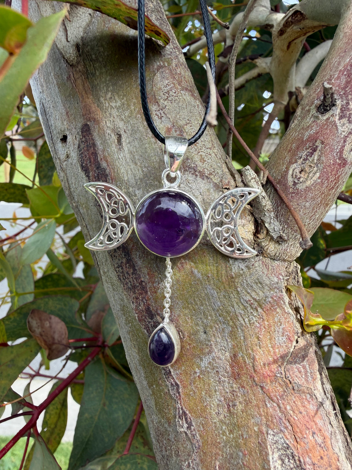 Triple moon amethyst pendant necklace photographed outdoors among natural greenery