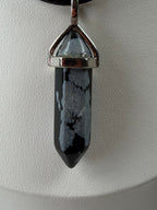 Close-up of a snowflake obsidian necklace crystal point pendant on a black cord