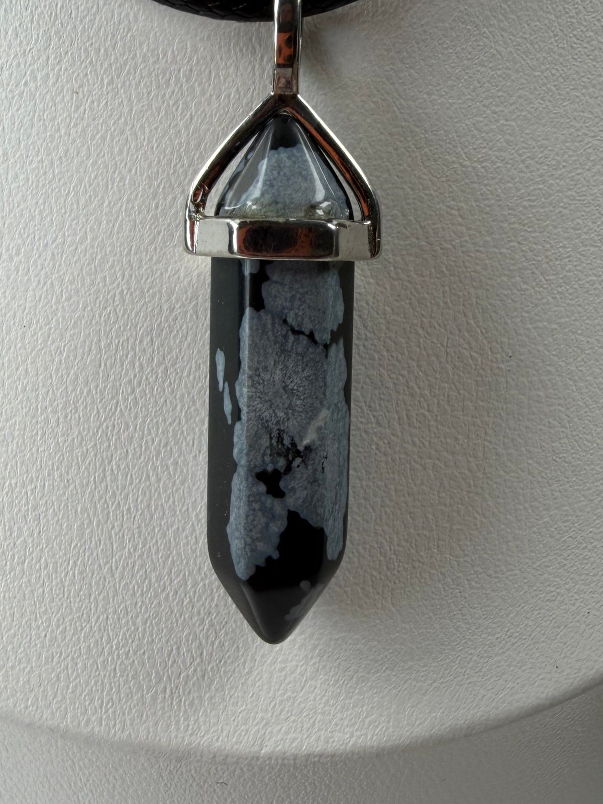 Close-up of a snowflake obsidian necklace crystal point pendant on a black cord