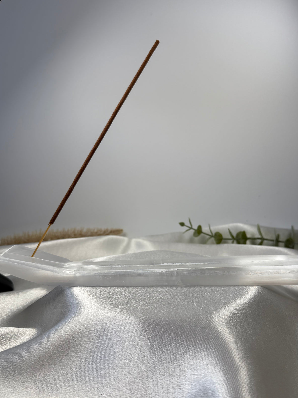 Natural selenite incense holder with a single incense stick on white fabric