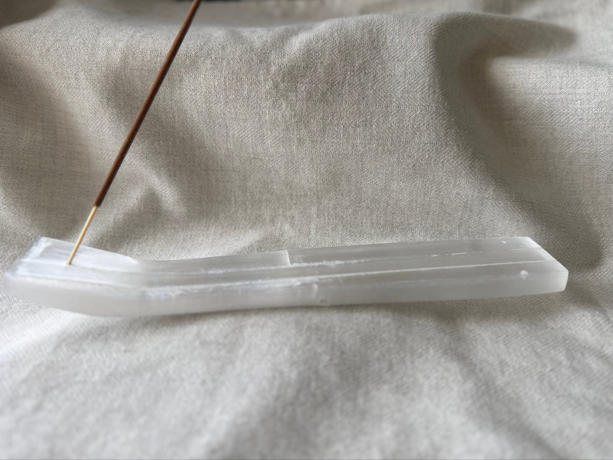 Translucent white selenite incense holder with a single incense stick on beige fabric