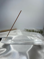 Natural selenite incense holder with a single incense stick on a white fabric surface