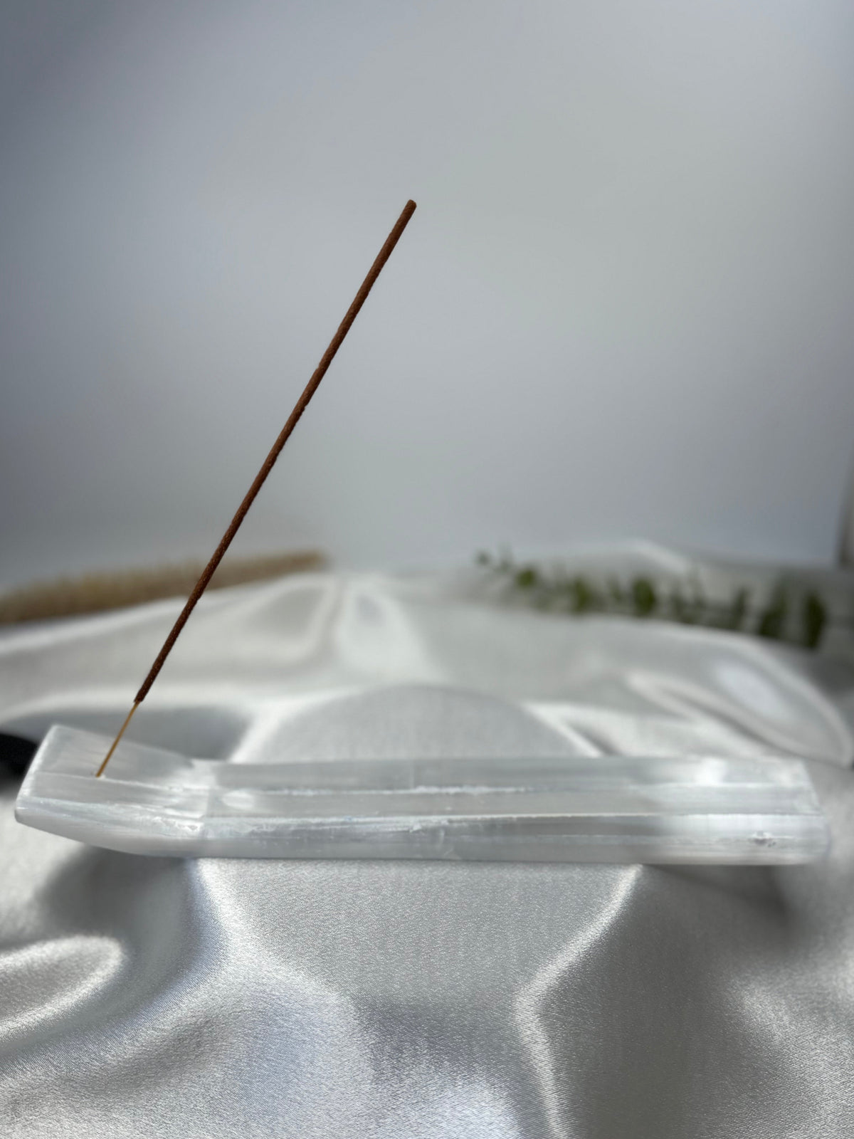 Natural selenite incense holder with a single incense stick on a white fabric surface