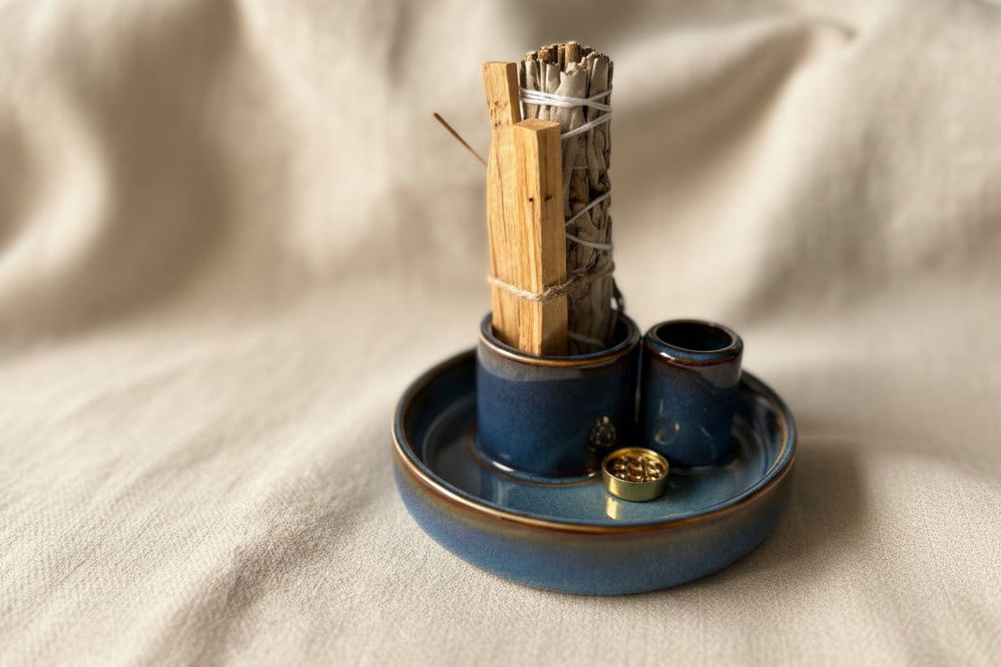smudge kit A blue ceramic incense holder with a bundle of dried herbs on a white linen cloth, with a blurred home background.
