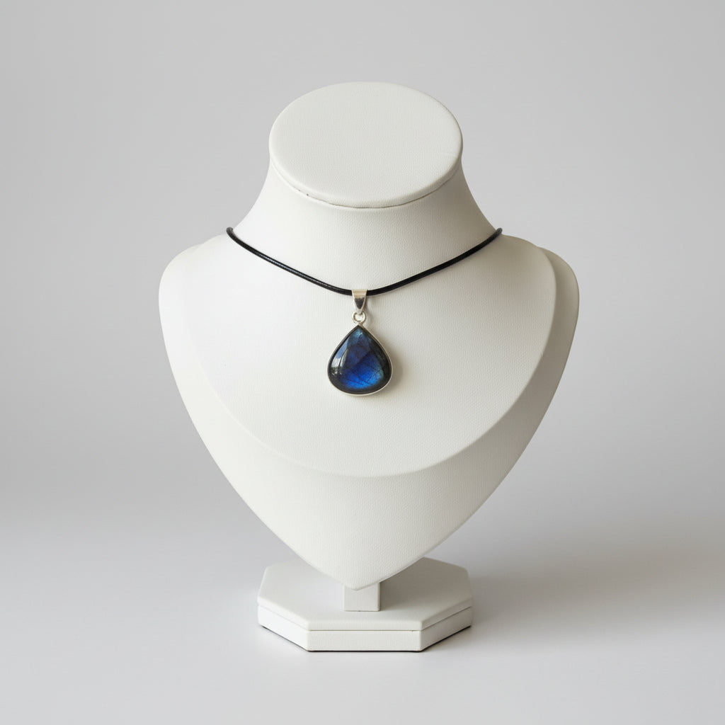 A silver-toned teardrop pendant necklace with a deep blue and black starry sky design, displayed on a cream-colored jewelry bust on a wooden stand.