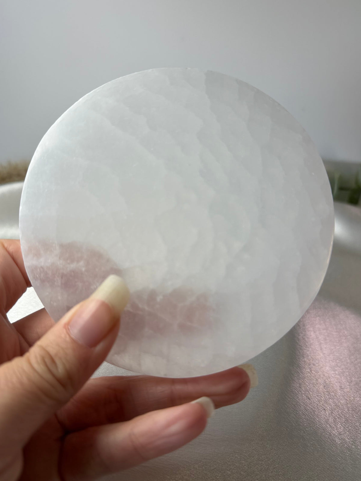 A hand holding a round, translucent white stone disc with a textured, cloudy surface.