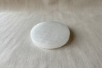 A round, faceted white stone or crystal ball resting on a textured beige fabric background.