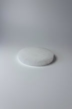 A round white textured stone or soap piece resting on a shiny silver satin fabric surface.