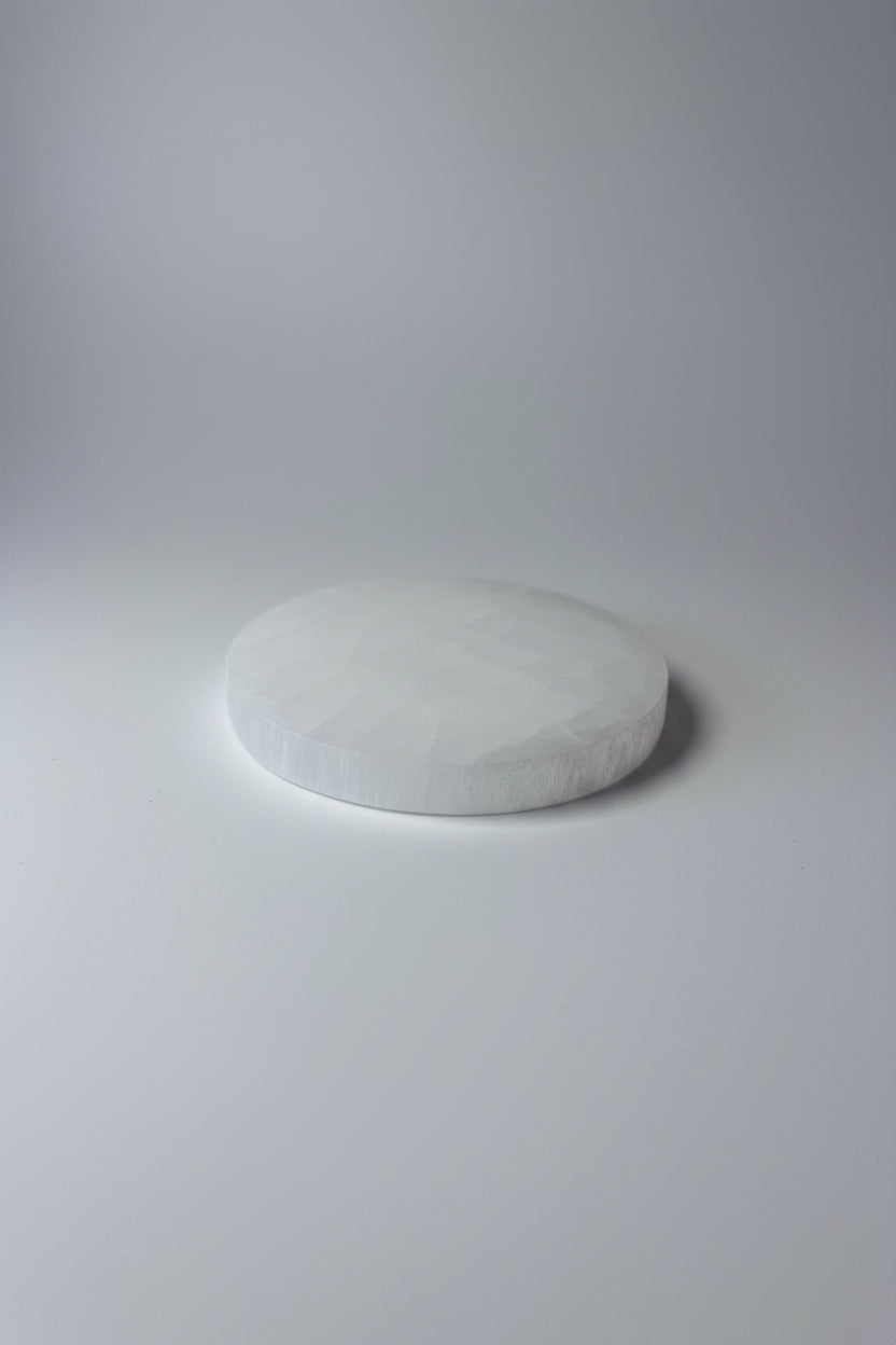 A round white textured stone or soap piece resting on a shiny silver satin fabric surface.