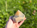 Treasured Energies agate crystal point with a polished top and natural raw base held in a hand outdoors.