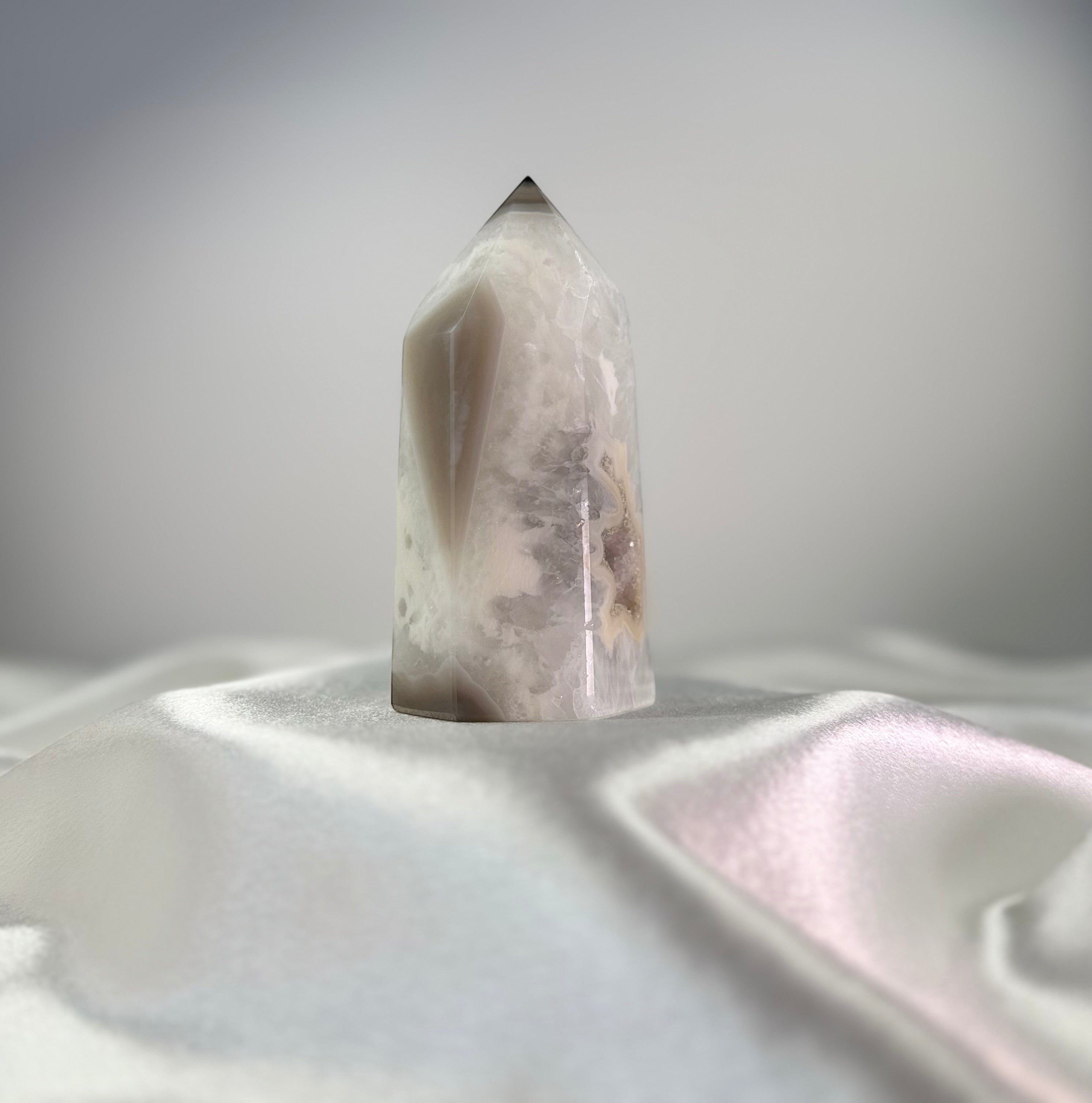 Treasured Energies white and black agate crystal point with sparkling druzy texture on a white satin fabric background.