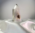 Treasured Energies polished agate crystal point with a white and black druzy geode center on a white satin fabric.