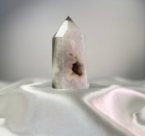 Treasured Energies polished agate crystal point with a white and black druzy geode center on a white satin fabric.