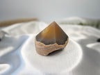 Treasured Energies agate crystal point with a polished top and natural banded base on white satin fabric.