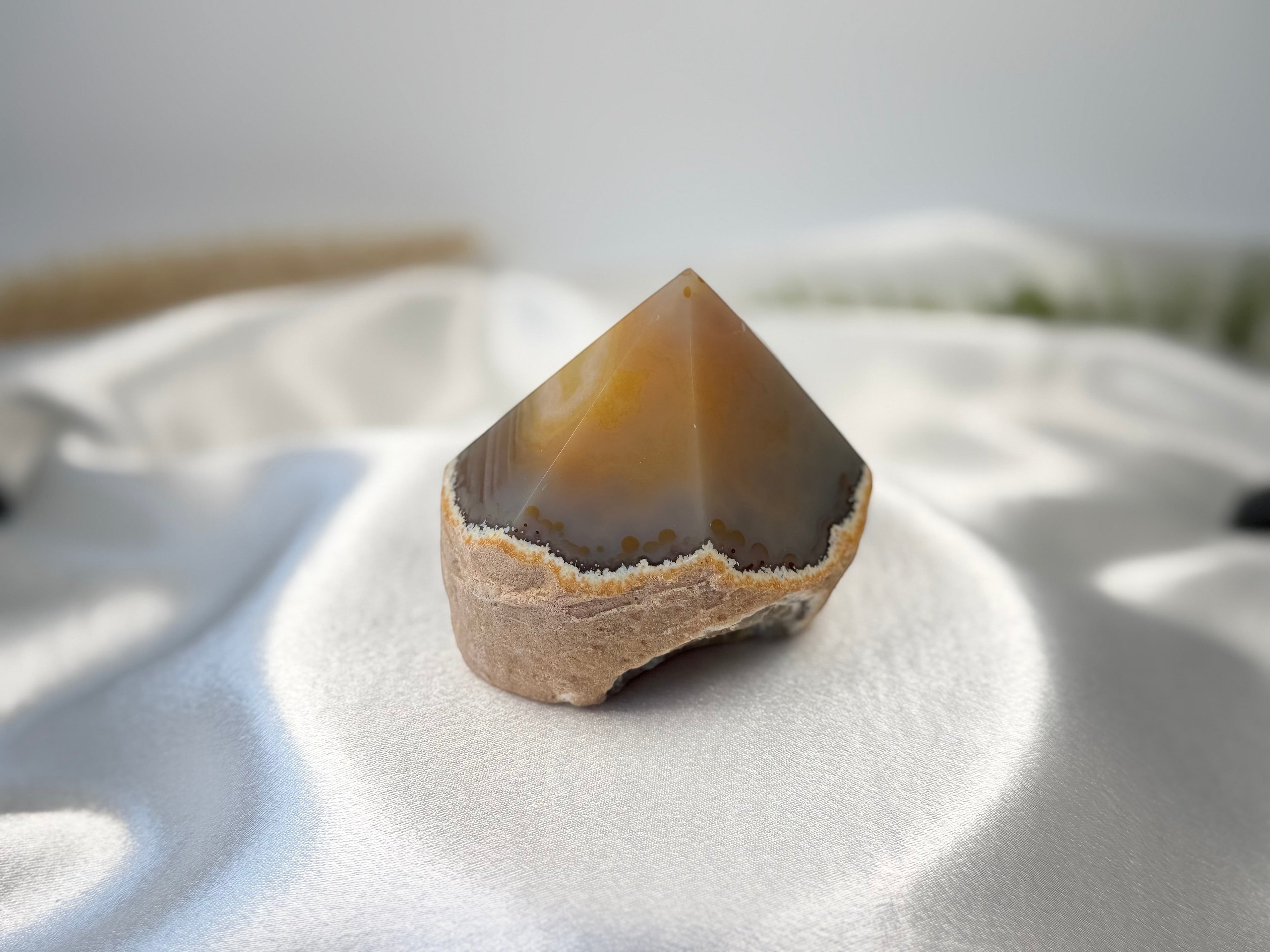Treasured Energies agate crystal point with a polished top and natural banded base on white satin fabric.