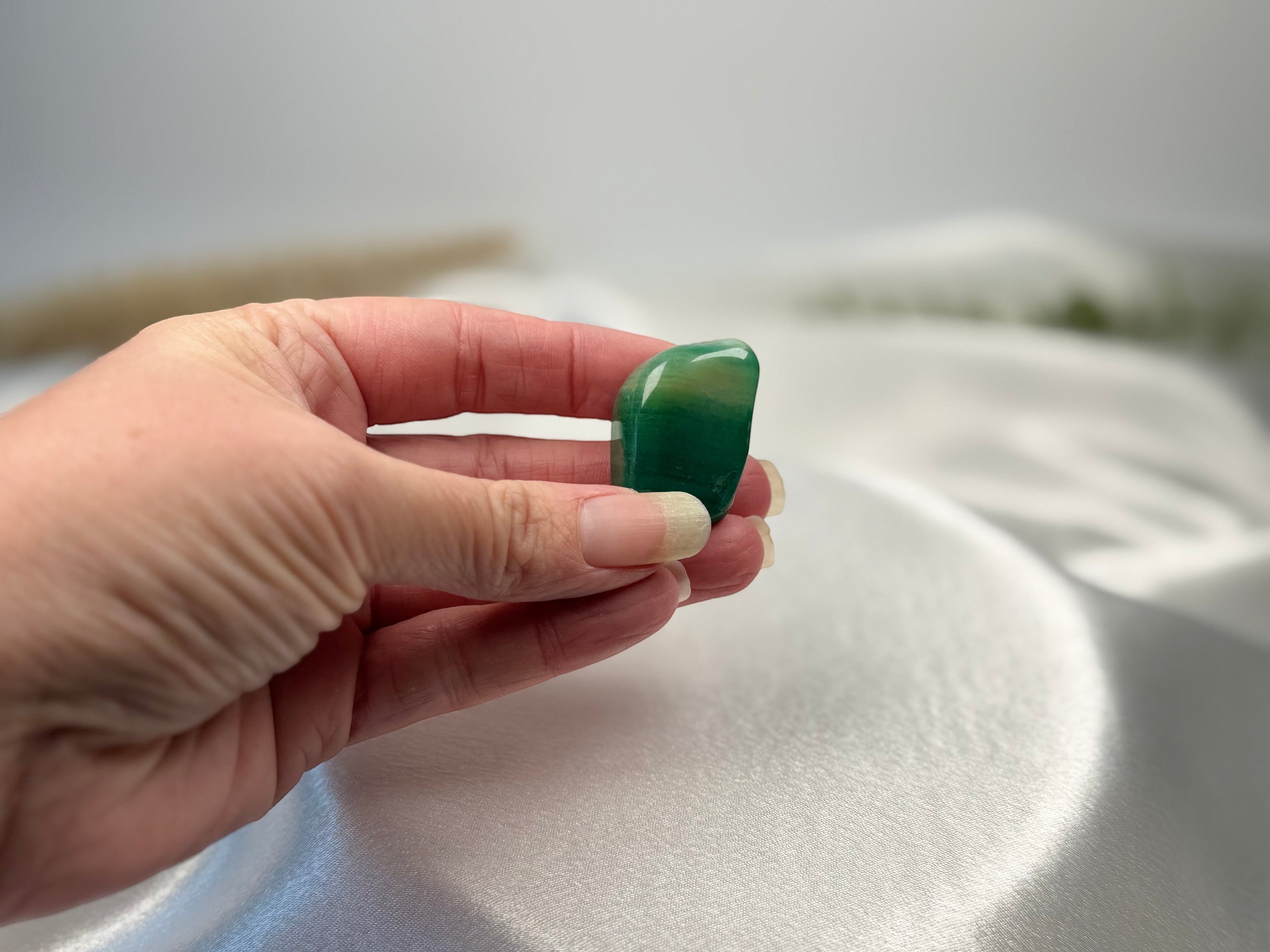 Treasured Energies polished Amazonite tumbled stone held in a hand against a soft white fabric background
