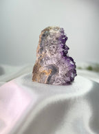 Treasured Energies freestanding amethyst crystal cluster with deep purple points on a white satin fabric background.