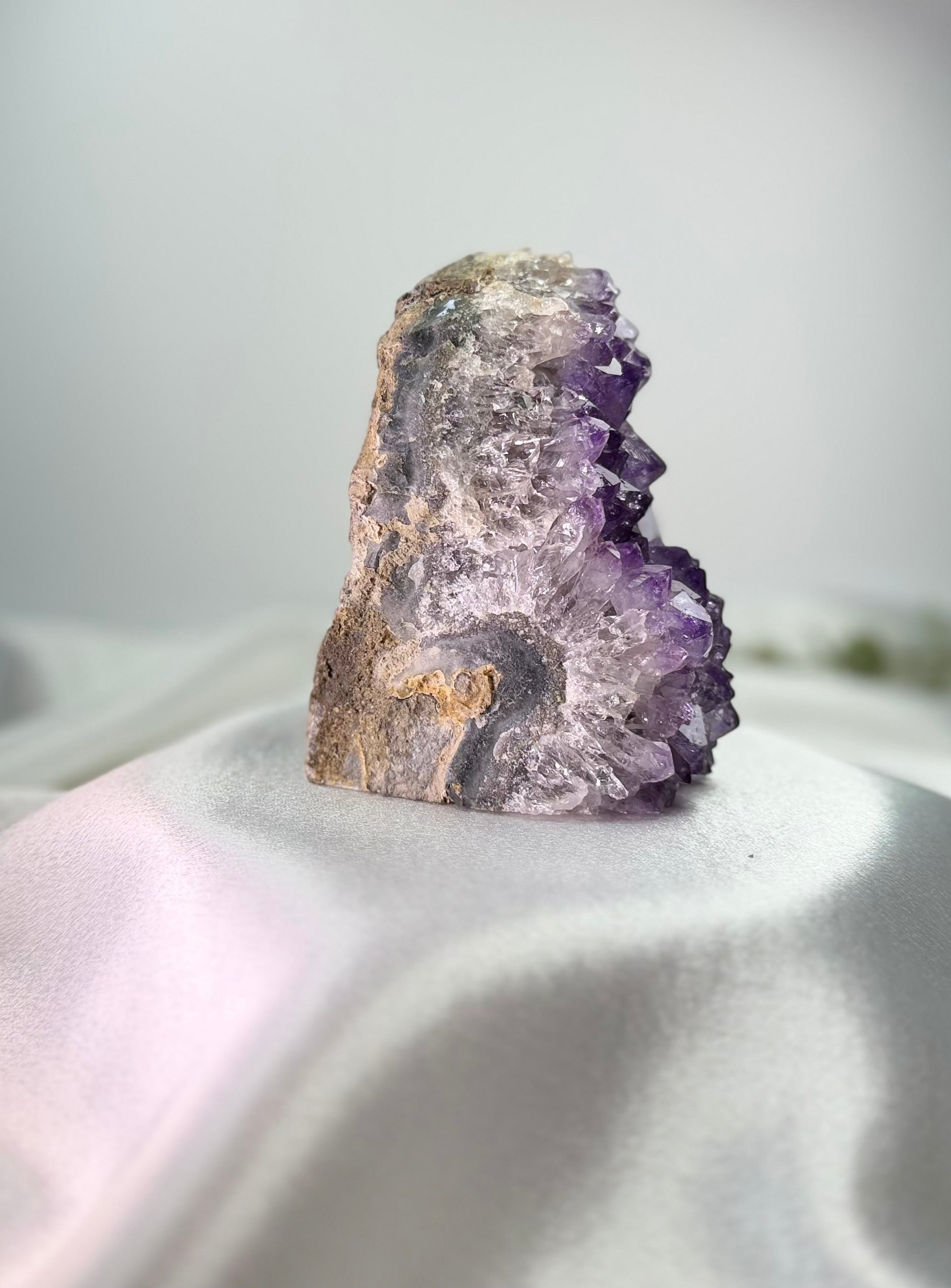 Treasured Energies freestanding amethyst crystal cluster with deep purple points on a white satin fabric background.