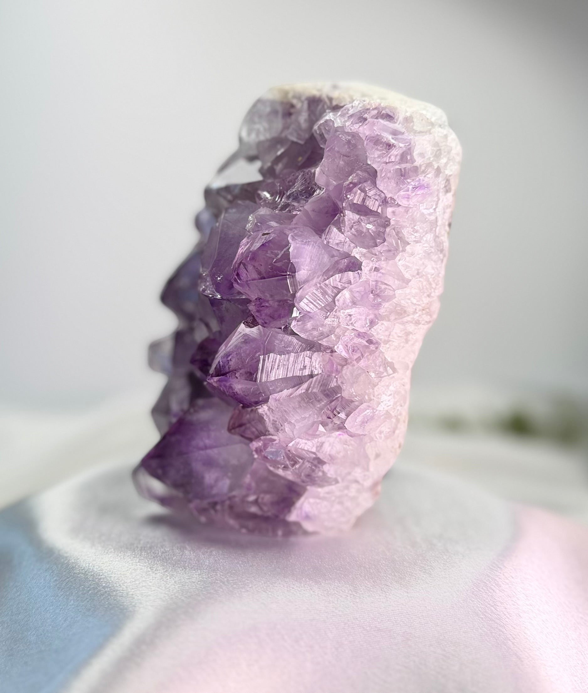 Treasured Energies natural amethyst crystal cluster with deep purple points on a white satin surface