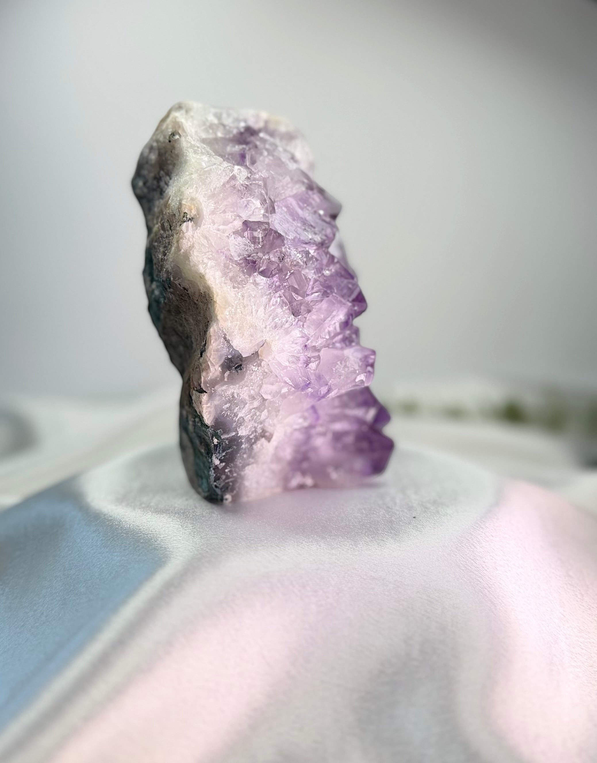 Treasured Energies natural amethyst crystal cluster with deep purple points on a white satin background