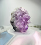 Treasured Energies natural amethyst crystal cluster with deep purple points on a white satin background