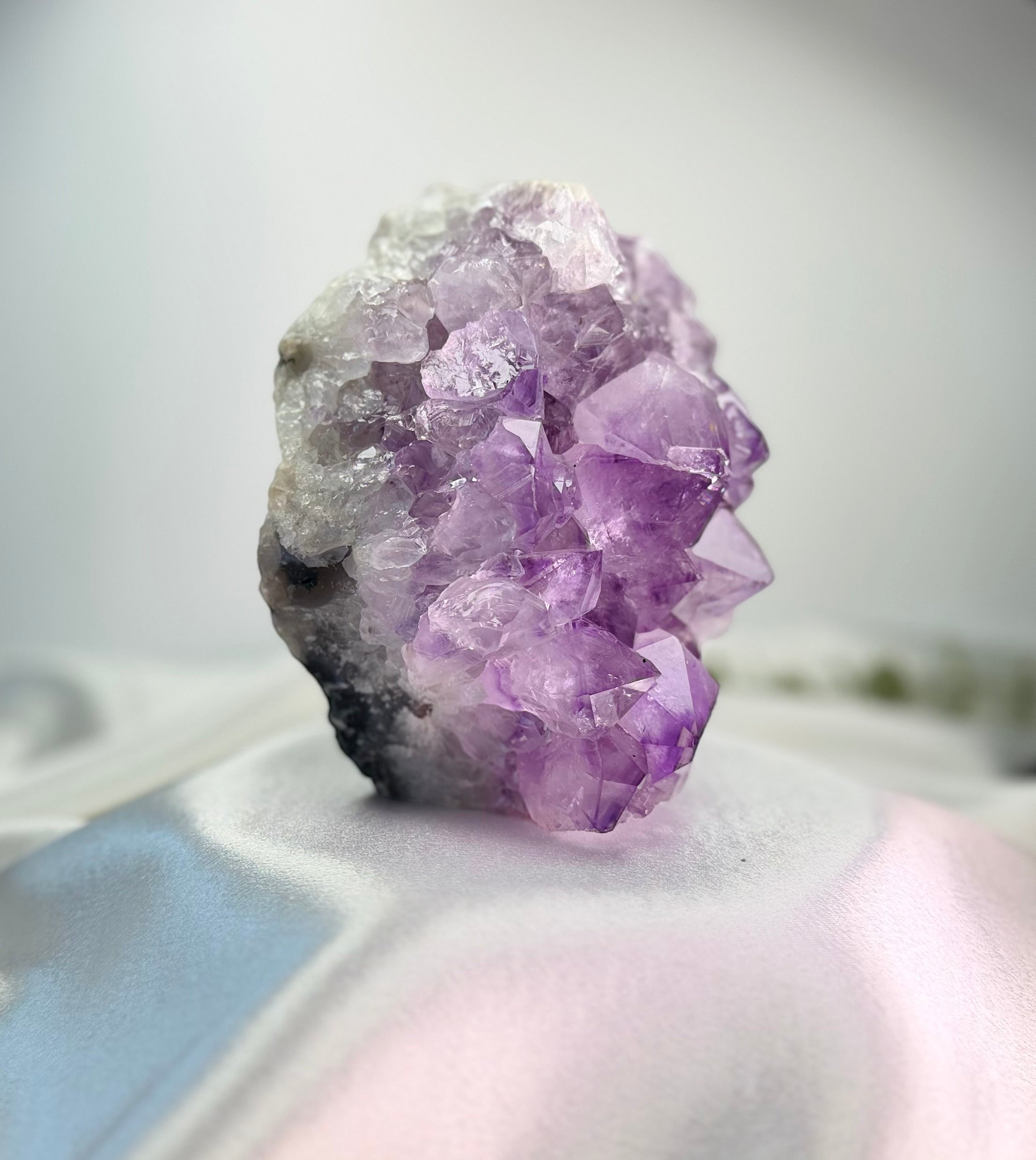 Treasured Energies natural amethyst crystal cluster with deep purple points on a white satin background