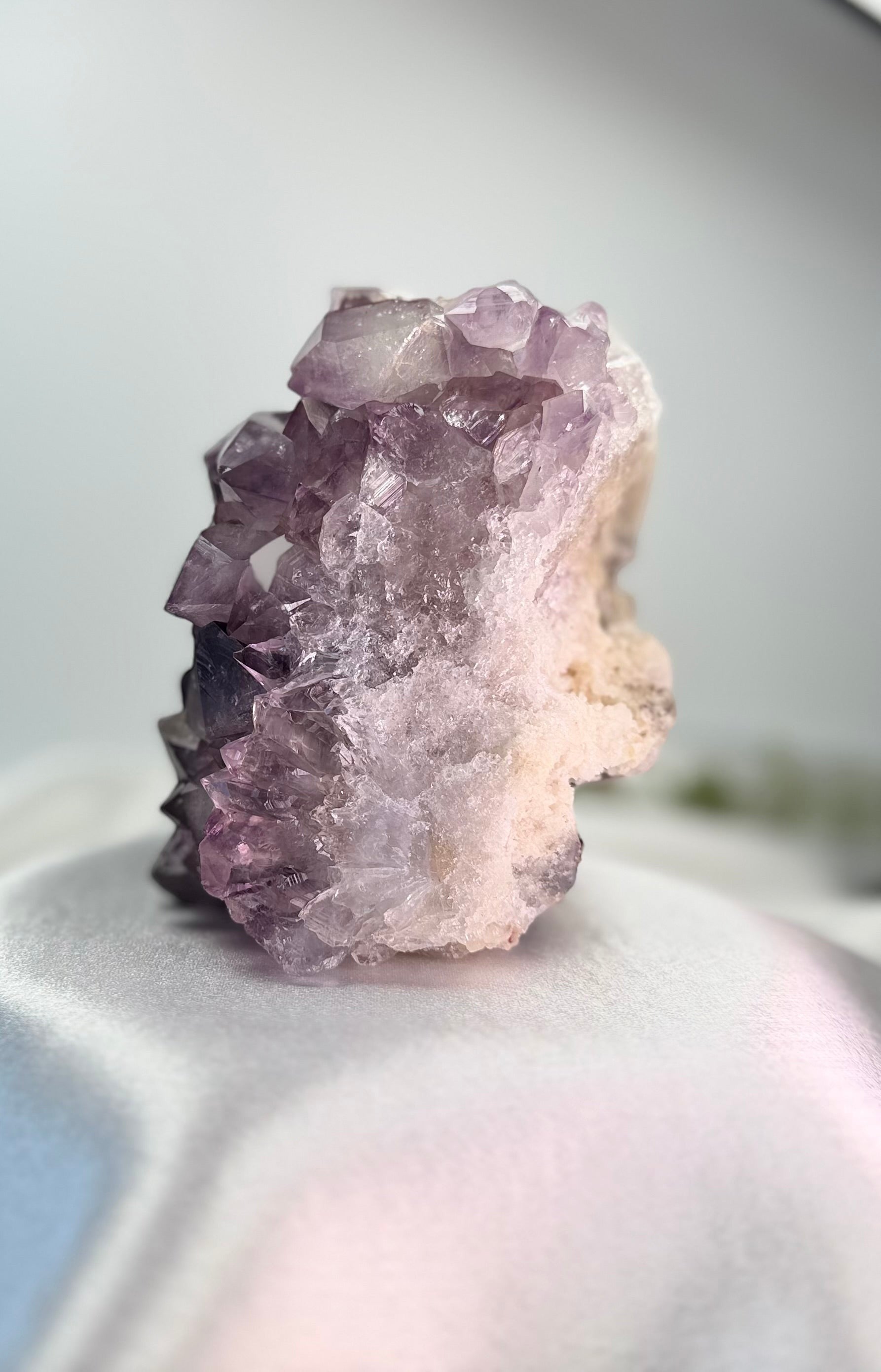 Treasured Energies natural amethyst crystal cluster with deep purple points and raw stone base on a white satin surface