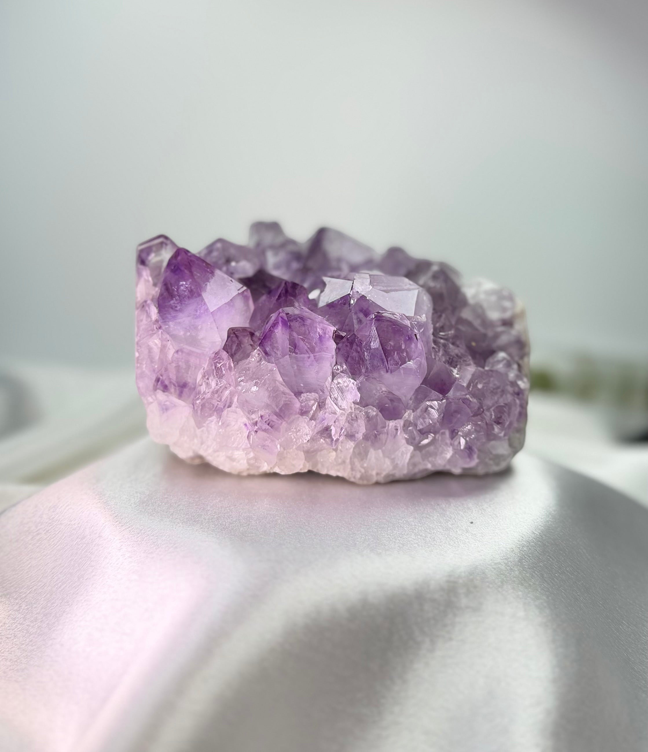 Treasured Energies natural purple amethyst crystal cluster specimen with pointed points on a white satin fabric background