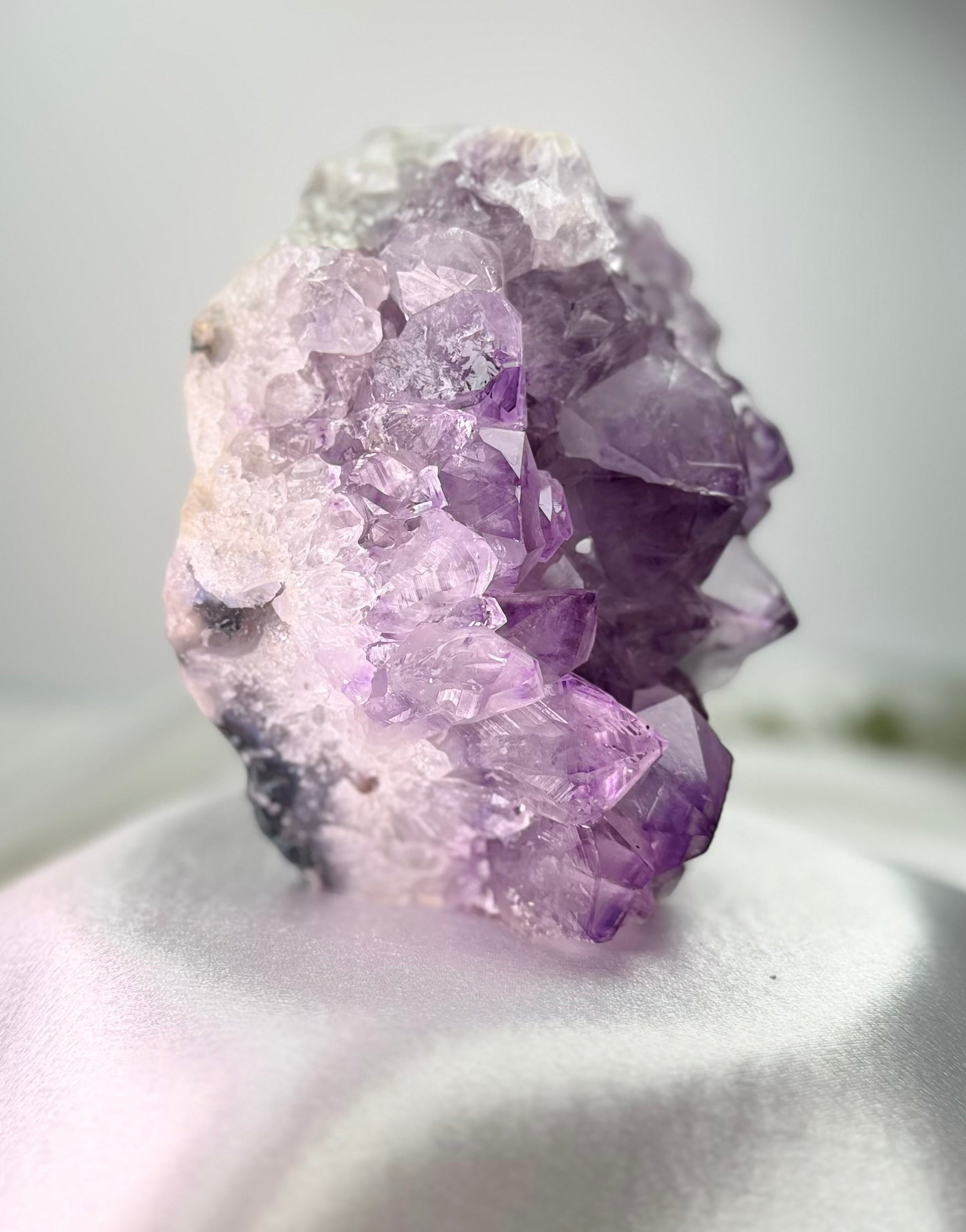 Treasured Energies natural amethyst crystal cluster with deep purple points on a white satin surface.