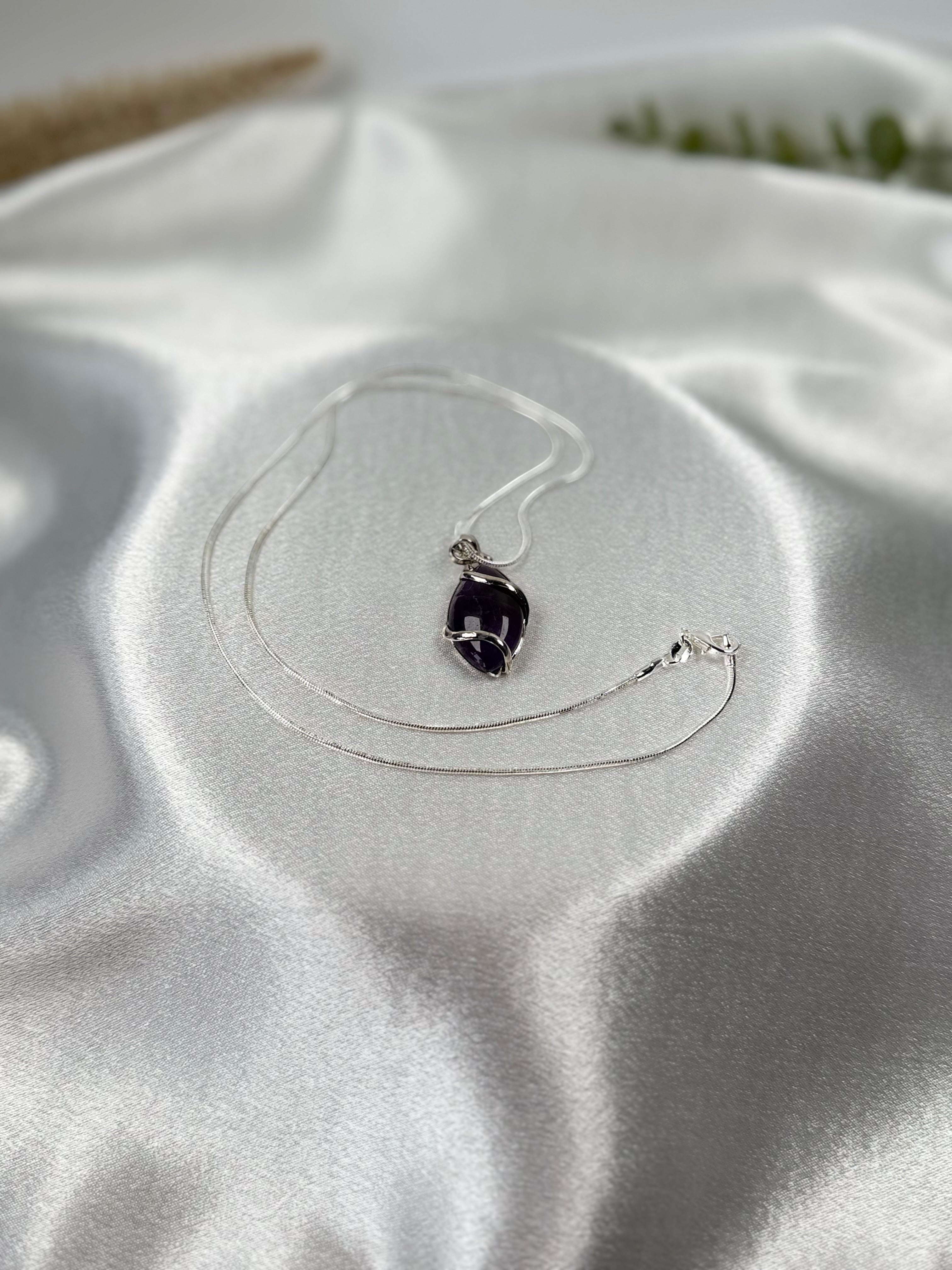 Treasured Energies amethyst crystal pendant necklace with silver wire wrapping on a white satin background