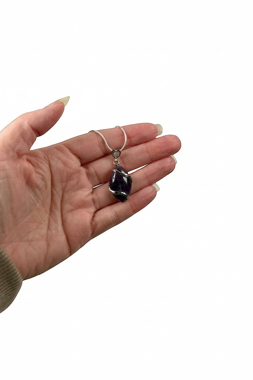 Treasured Energies amethyst natural crystal pendant wrapped in silver wire, held in a palm against a white background.