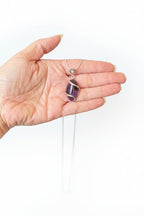 Treasured Energies amethyst crystal pendant wrapped in silver wire with a heart-shaped bail held in a hand