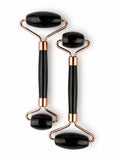Treasured Energies dual-ended black obsidian facial massage rollers with rose gold metal hardware on a white background.