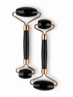 Treasured Energies dual-ended black obsidian facial massage rollers with rose gold metal hardware on a white background.