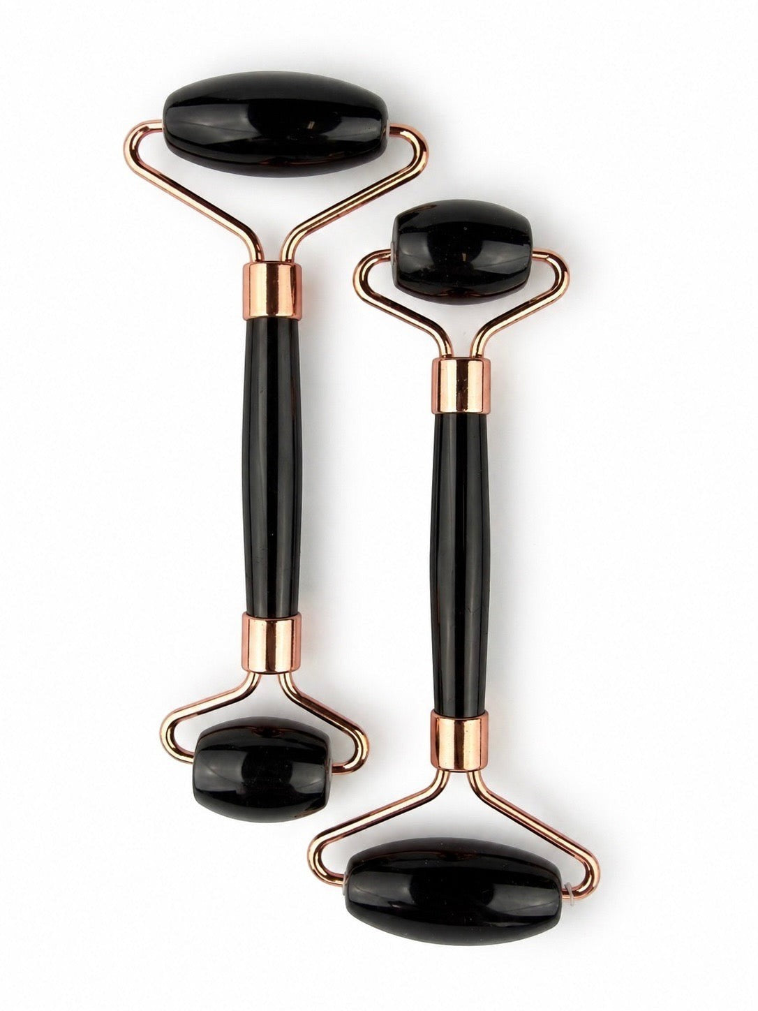 Treasured Energies dual-ended black obsidian facial massage rollers with rose gold metal hardware on a white background.
