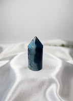 Treasured Energies blue agate crystal tower with a polished point and natural banded texture on white silk fabric.
