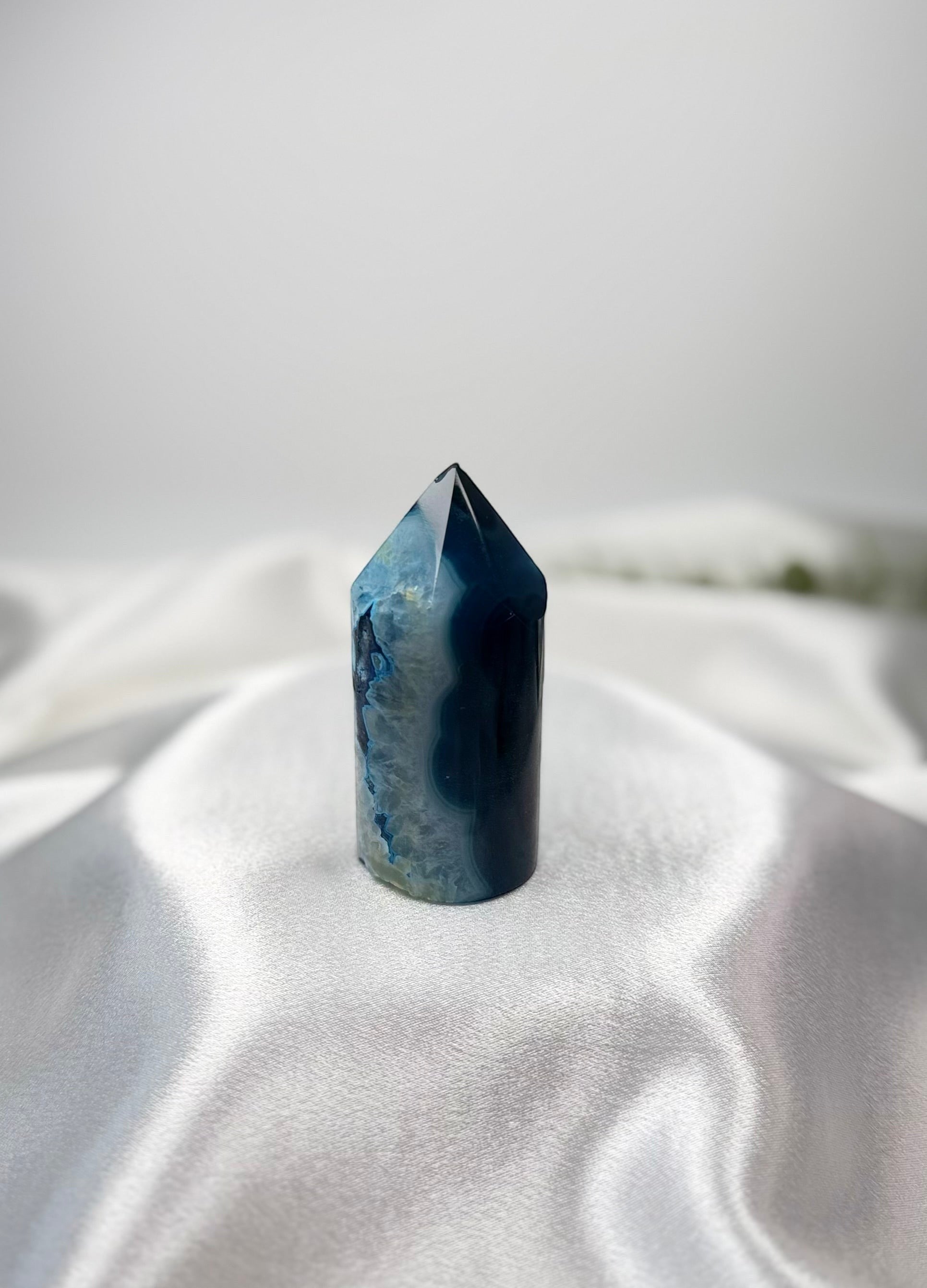 Treasured Energies blue agate crystal tower with a polished point and natural banded texture on white silk fabric.