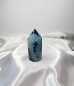 Treasured Energies blue agate crystal tower with a polished point and natural geode center on a white satin fabric.