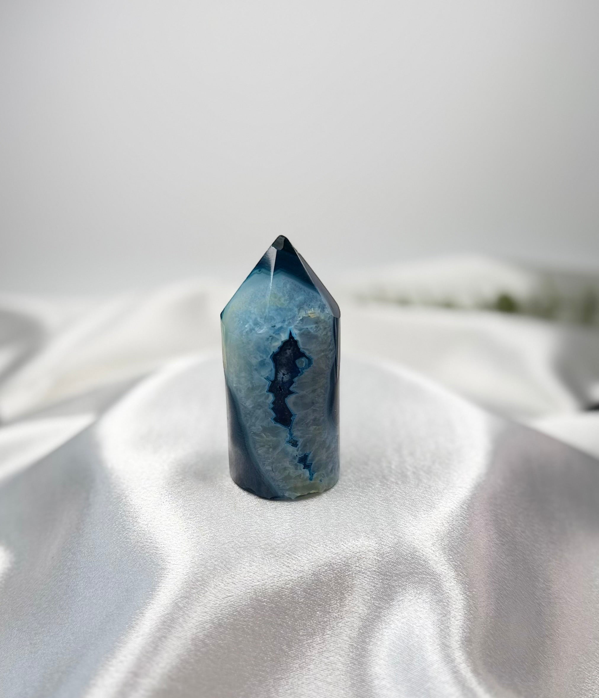 Treasured Energies blue agate crystal tower with a polished point and natural geode center on a white satin fabric.