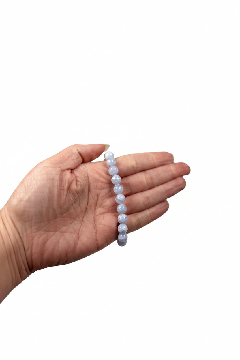 Treasured Energies blue lace agate crystal bead bracelet held in a hand against a soft white satin background