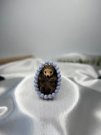 Treasured Energies blue lace agate crystal bead bracelet encircling a small brown hedgehog figurine on satin fabric