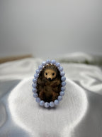 Treasured Energies blue lace agate crystal bead bracelet encircling a small decorative hedgehog figurine on satin