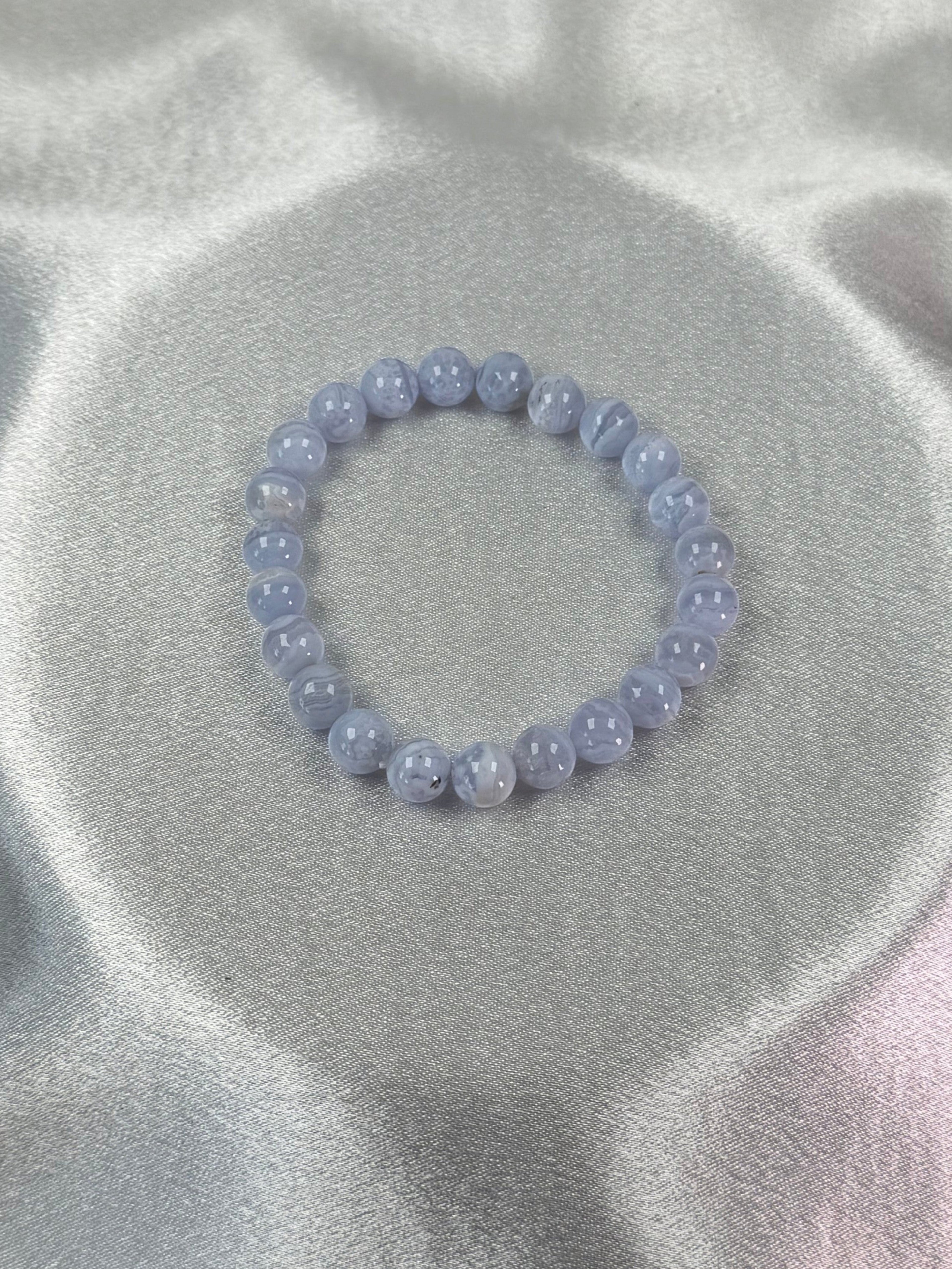Treasured Energies blue lace agate crystal bead bracelet on a smooth white satin fabric background