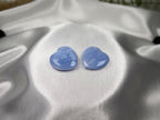 Two polished Blue Lace Agate crystal hearts from Treasured Energies displayed on smooth white satin fabric.