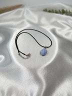 Treasured Energies blue lace agate pendant necklace with a matte finish on a black cord against white satin fabric.