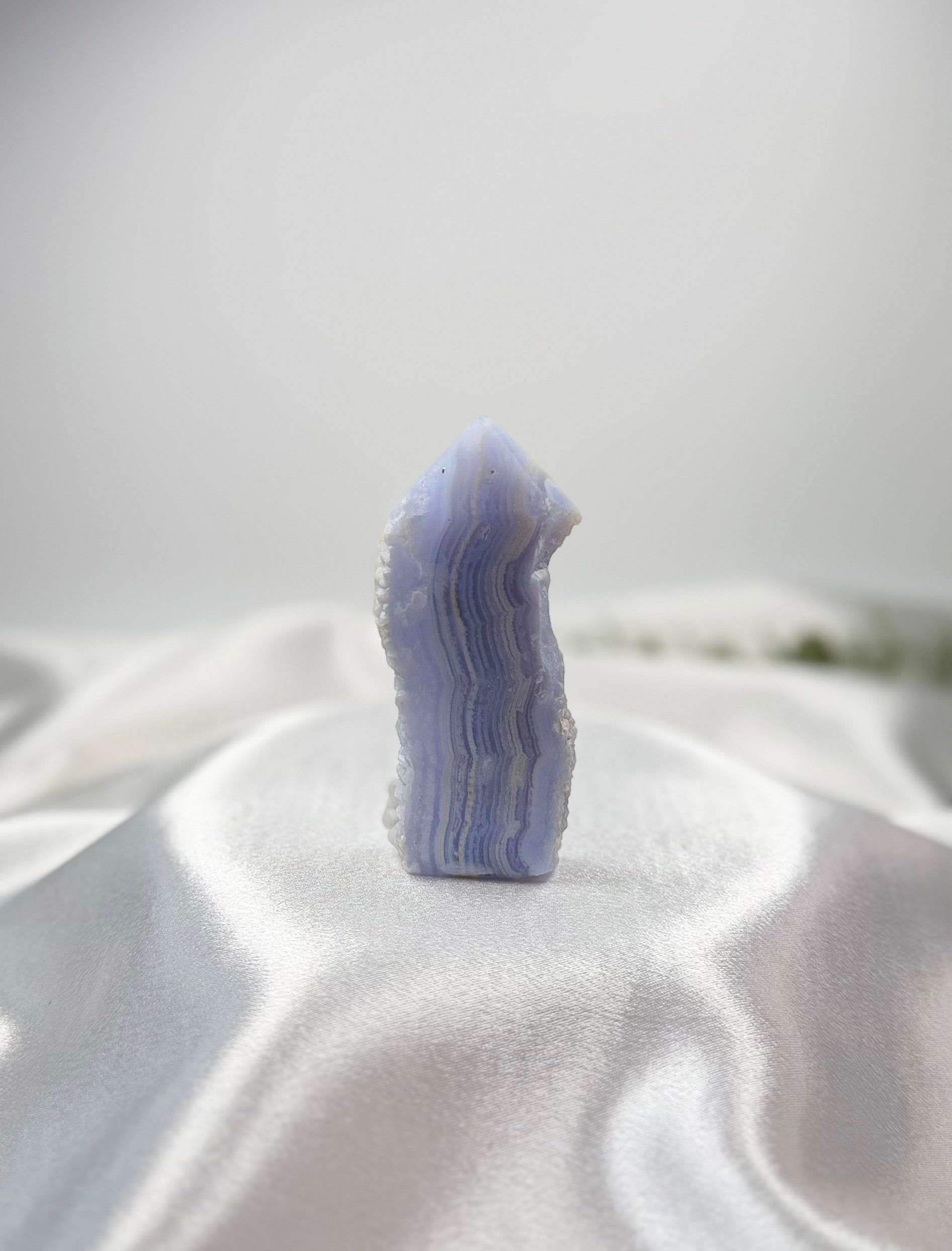 Treasured Energies Blue Lace Agate tower point with delicate light blue and white banded layers on white satin fabric.