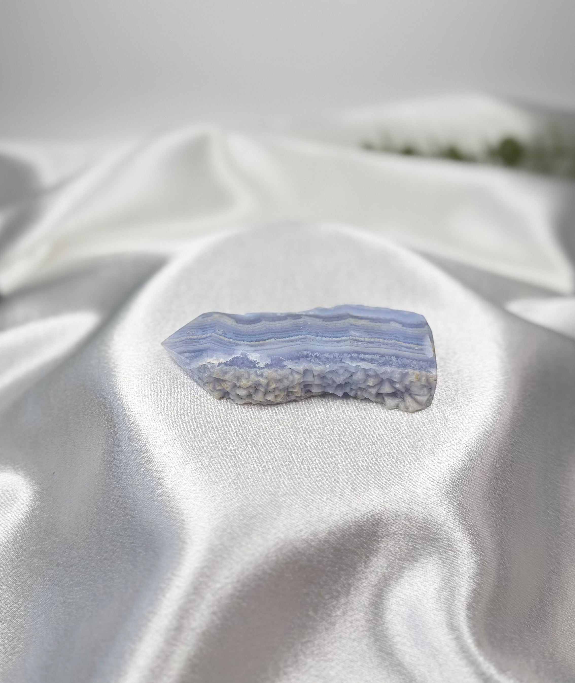 Treasured Energies Blue Lace Agate tower point with delicate blue and white banding on a soft white satin background.