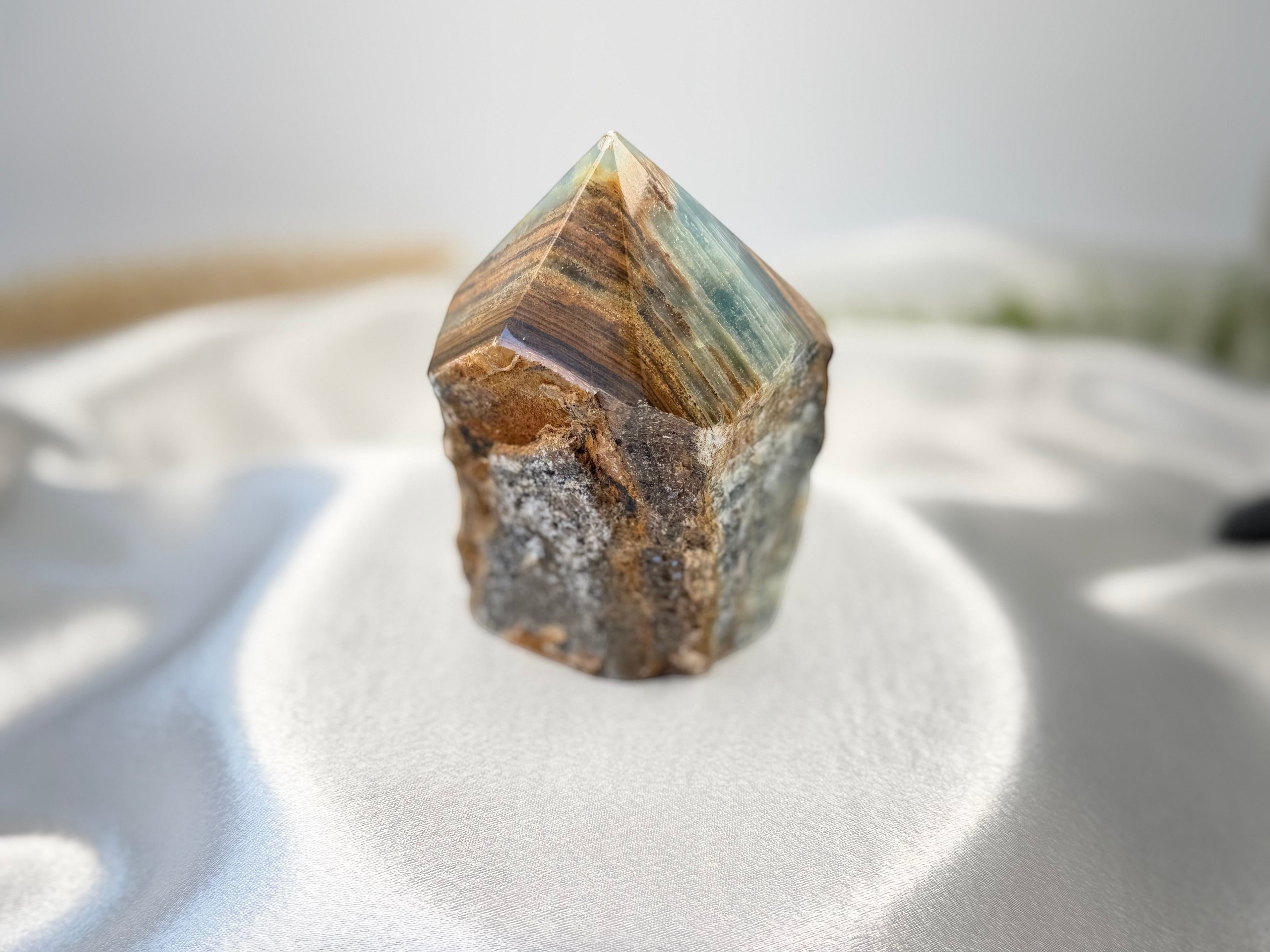Treasured Energies Blue Onyx crystal tower with a polished point and raw, natural base on a white satin background.