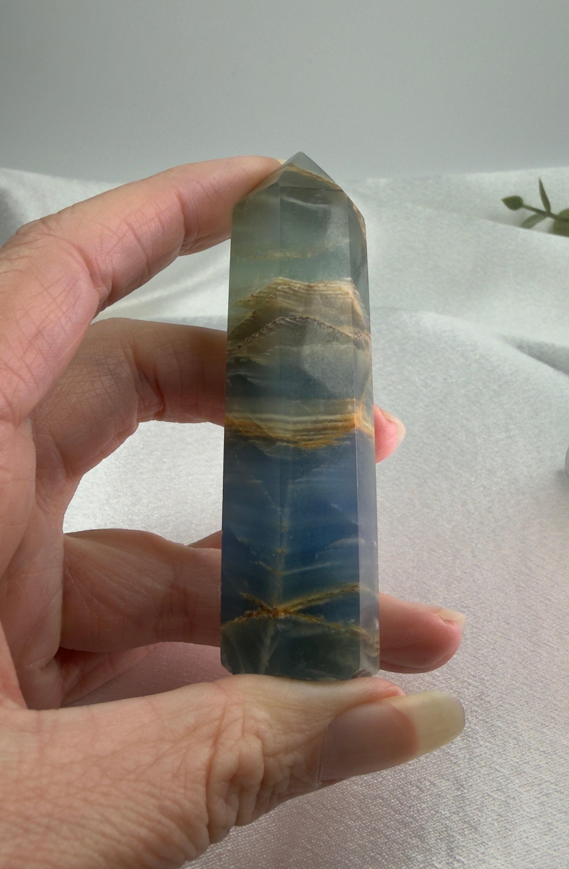 Treasured Energies polished blue onyx crystal tower held in hand, showing natural blue banding and earthy inclusions.
