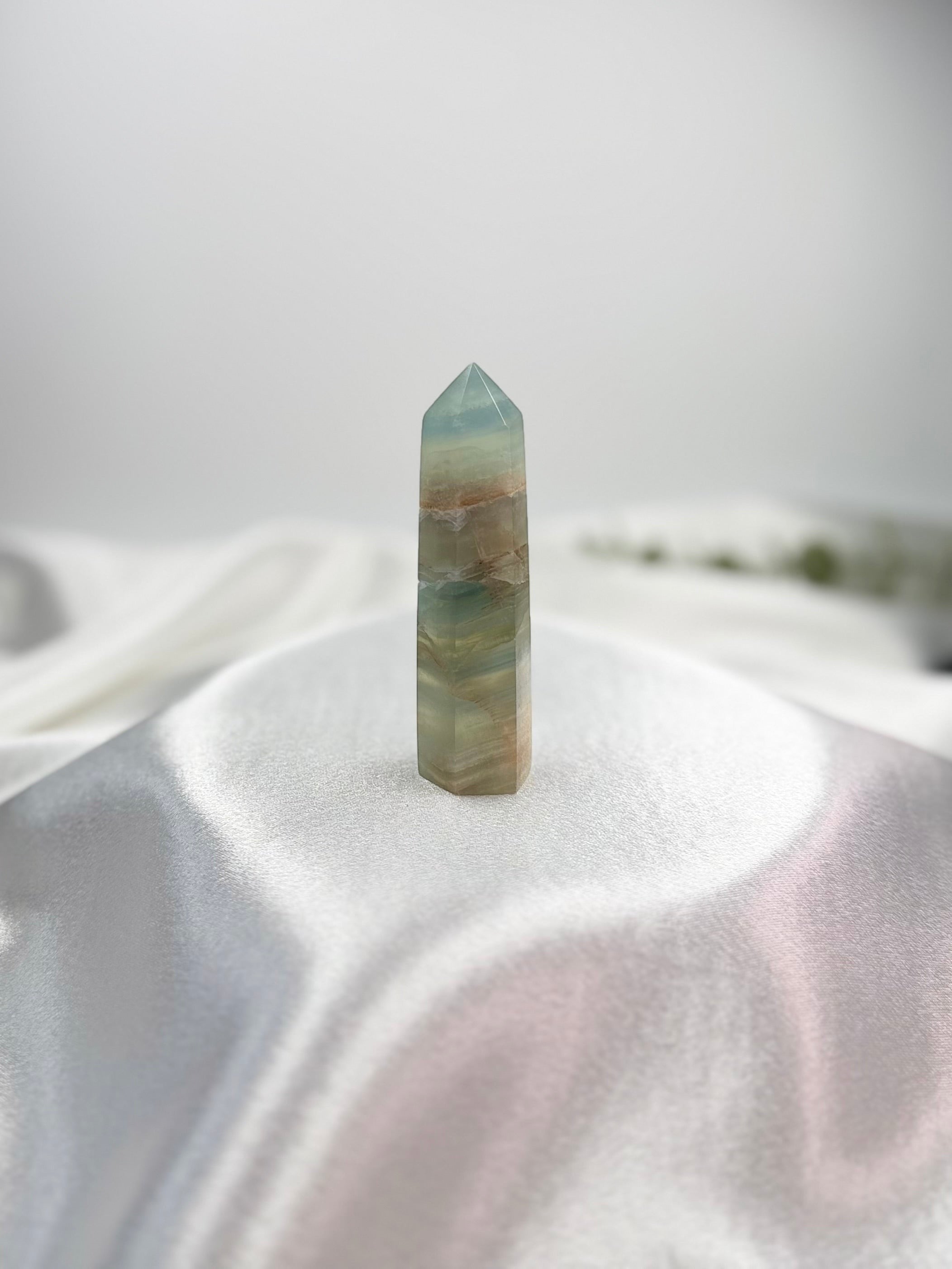 Treasured Energies Blue Onyx crystal tower with polished finish and natural banding on a white satin fabric background.